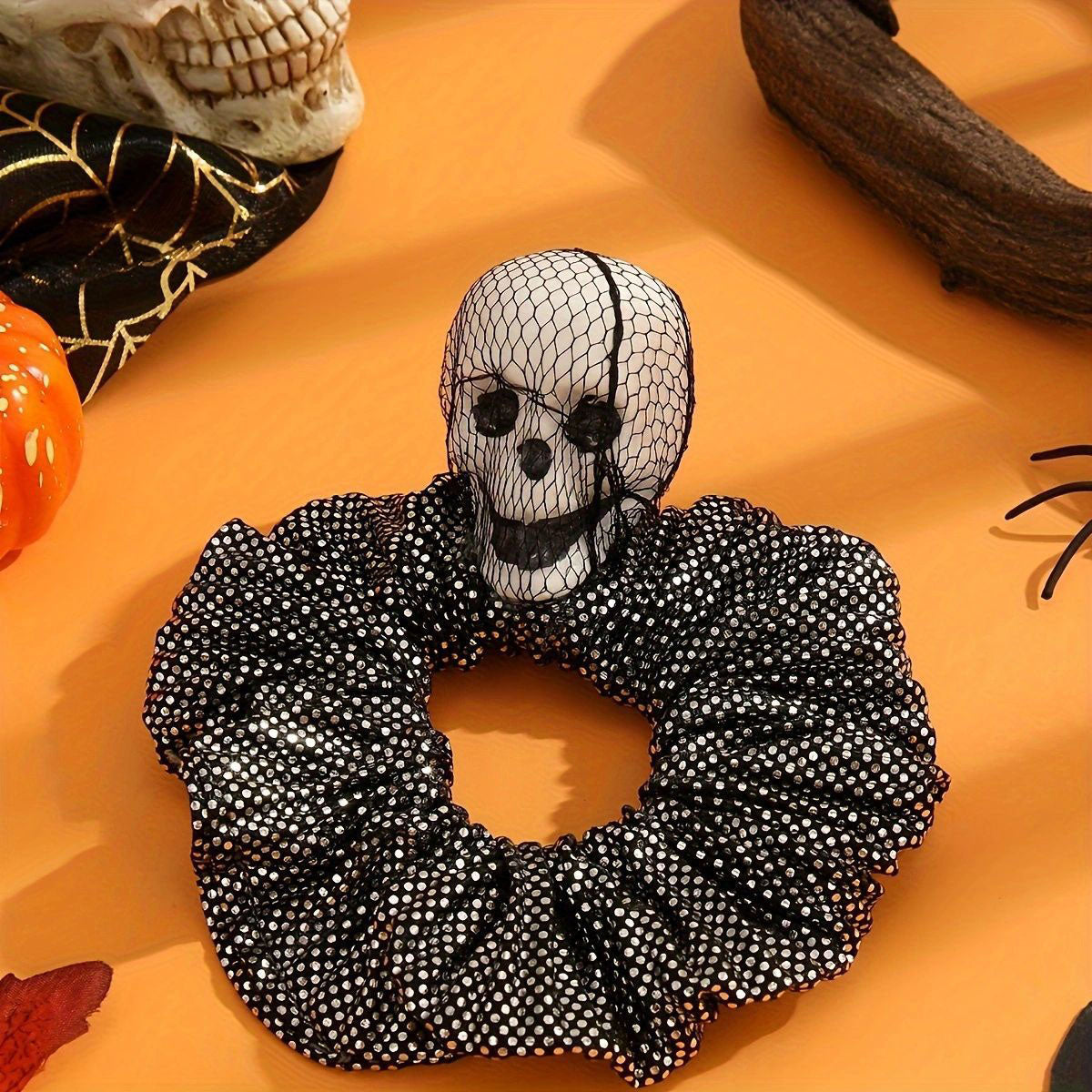 A close-up of a black Halloween-themed scrunchie featuring a prominent white 3D skull decoration, perfect for punk and gothic styles.