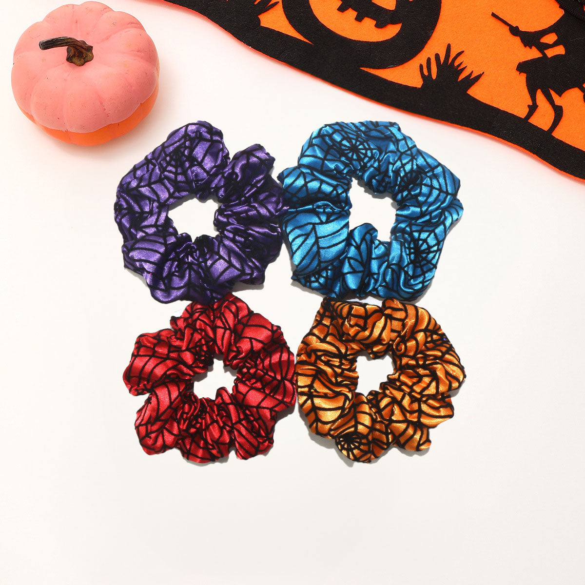 A set of four colorful Halloween-themed silk hair scrunchies with spiderweb patterns, displayed on a white background.