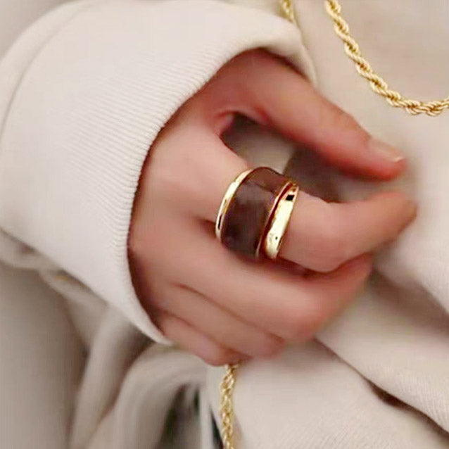 A close-up of a hand wearing two brass cuff rings with a chunky, dual-layered chocolate enamel design, part of a stylish set of five.