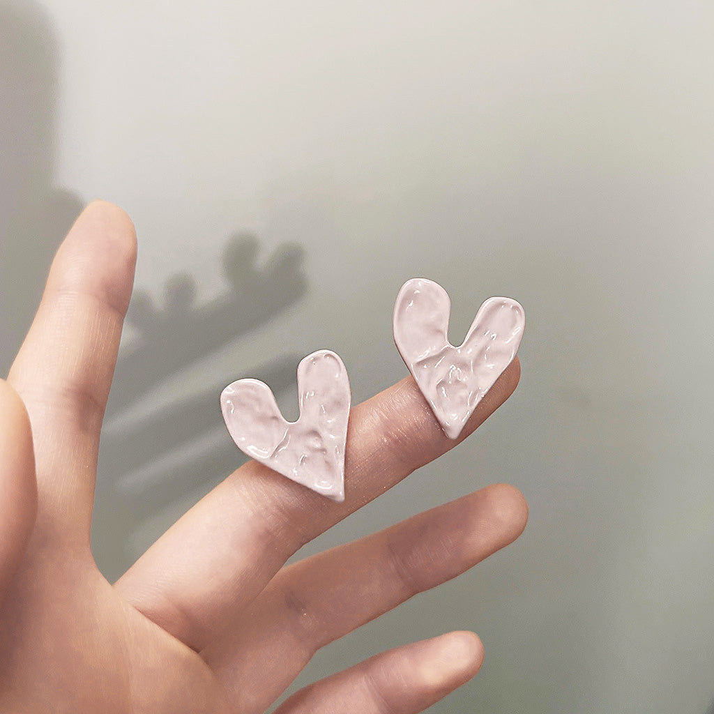 A pair of wholesale pink enamel heart-shaped stud earrings with a hammered texture, displayed on a white background.