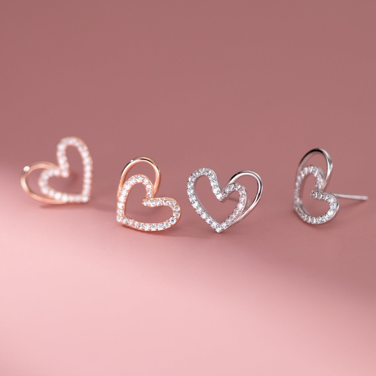 A set of 925 silver hollow-out heart stud earrings, showcasing both rose gold and silver finishes with sparkling gemstone details.