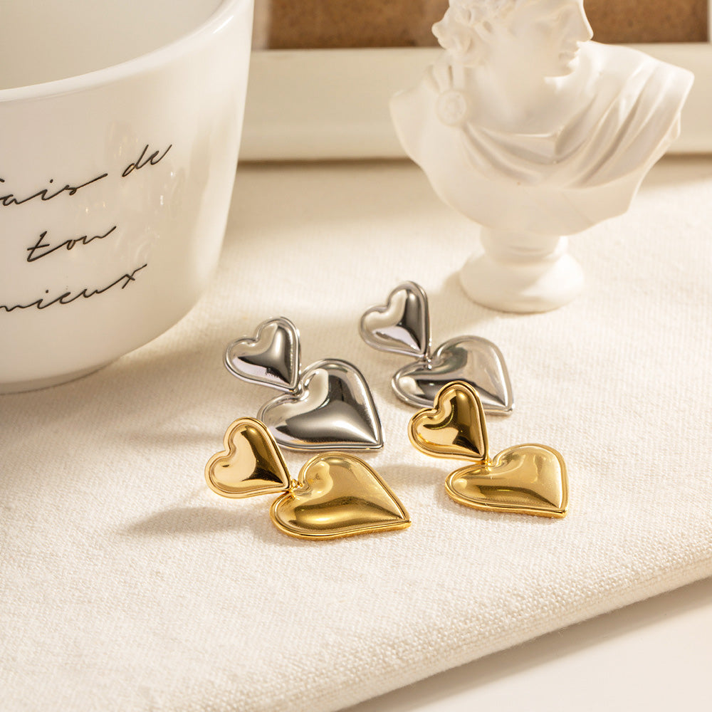 A stylish display of stainless steel double heart statement drop earrings in both gold and silver, presented with elegant decorative props.