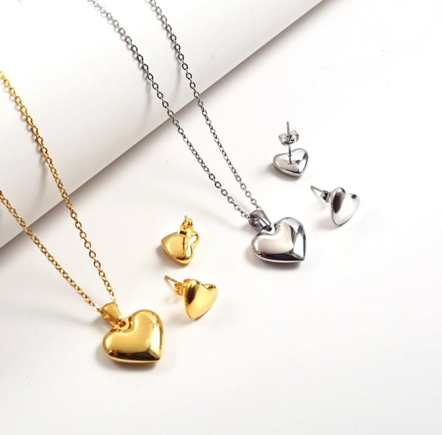 A beautiful stainless steel heart charm jewelry set, available in both polished gold and silver finishes, featuring a matching necklace and stud earrings.