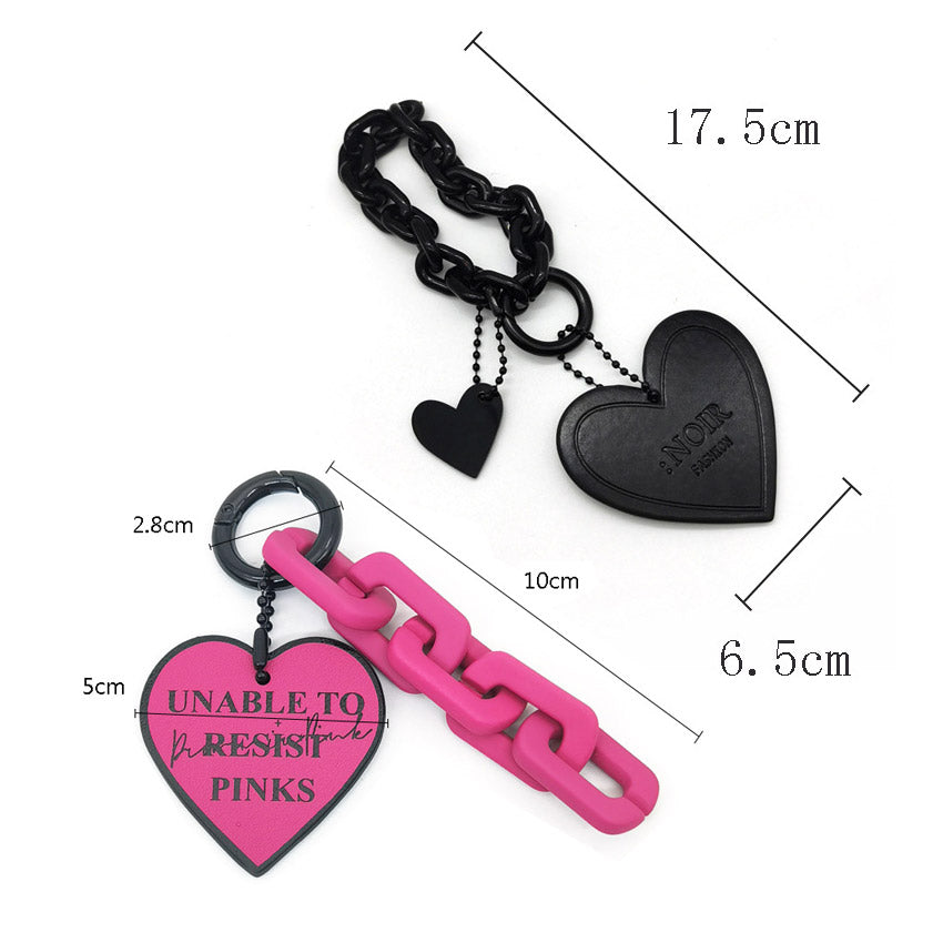 A pair of stylish PU leather heart-shaped bag charm keychains, one in black and one in pink, with metal chain attachments.