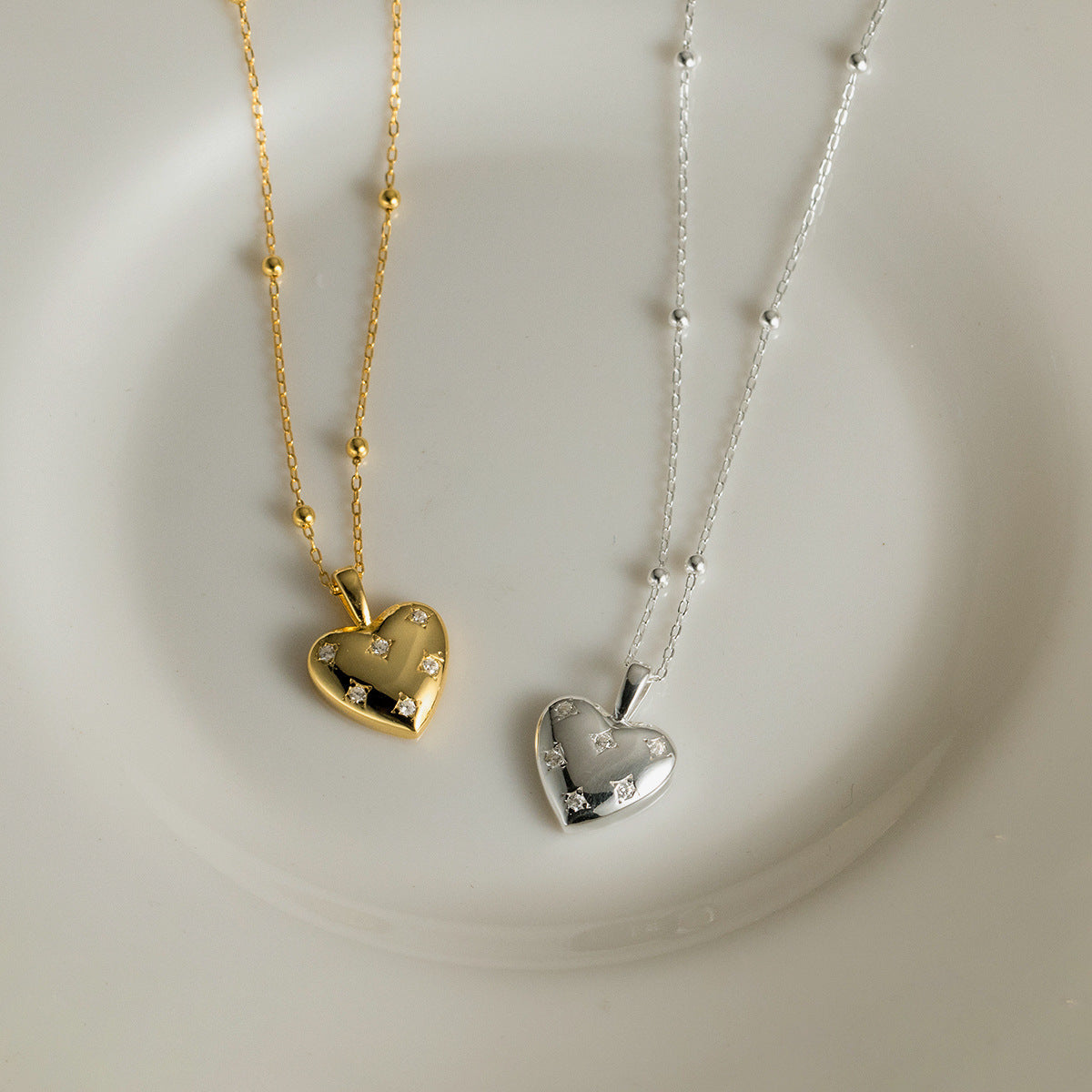 A stunning pair of S925 sterling silver heart pendant necklaces, one in a polished silver finish and the other in a warm gold finish, both embellished with sparkling cubic zirconia stones.