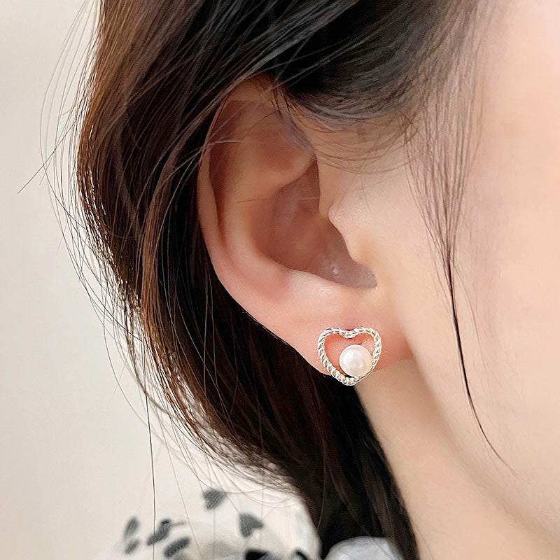 A close-up of a woman wearing the 925 sterling silver hollow heart pearl stud earring, showcasing its elegant design and pearl accent.