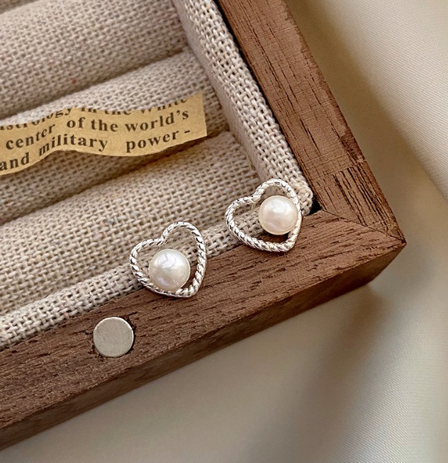 A pair of 925 sterling silver heart-shaped earrings with a central pearl, elegantly displayed inside a wooden jewelry box.