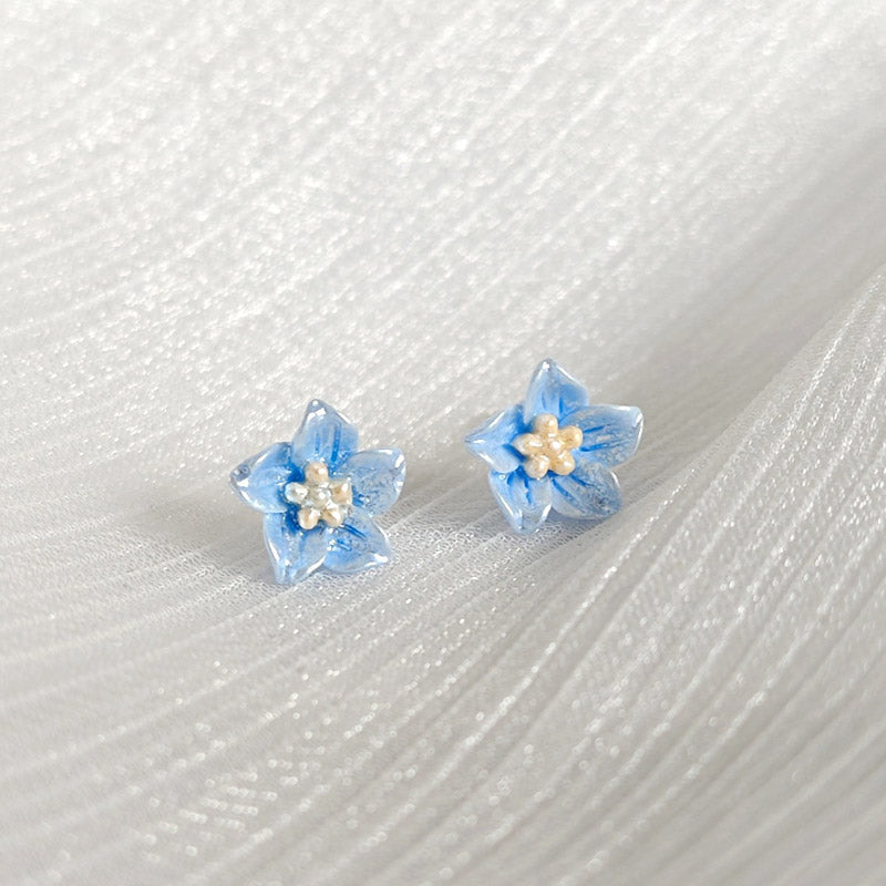 A pair of light blue resin small floral flower stud earrings with white centers, shown on a clean white background.