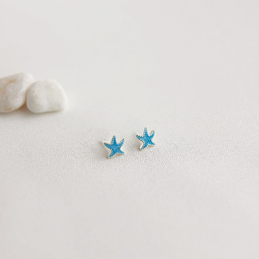 A pair of silver-plated tiny blue enamel starfish stud earrings on a clean white background, showcasing their detailed design and vibrant color.