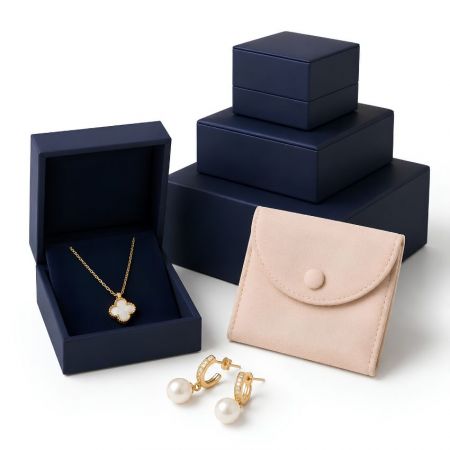 Stacked navy blue wholesale jewelry boxes in multiple sizes with a pink microfiber button pouch and pearl earrings.