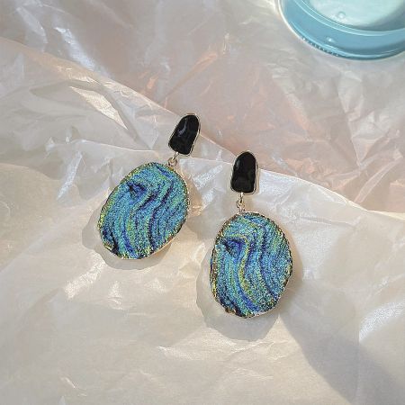 Close-up of a drop earring with an iridescent abalone shell-inspired design and gold trim.