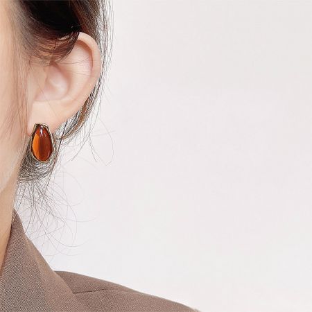 Close-up of a model wearing an amber-colored asymmetric stud earring.