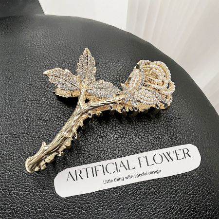 A beautiful gold rose hair clip with delicate rhinestone and pearl details on a black background.