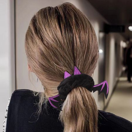 A model's ponytail styled with a black and purple glittery bat wing hair scrunchie.