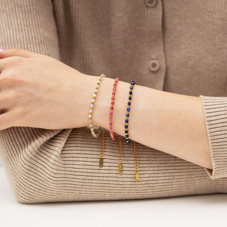 A wrist showcasing three dainty stacking bracelets with vibrant beads and gold accents.