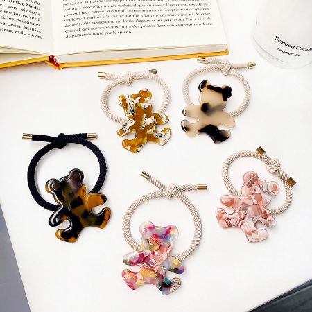 An assortment of bear-shaped charm hair ties in various colors and patterns, including tortoiseshell and solid pink.