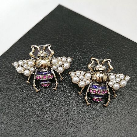 A detailed view of two bee brooches, focusing on the texture of the pearl-studded wings and the sparkle of the gemstone accents.