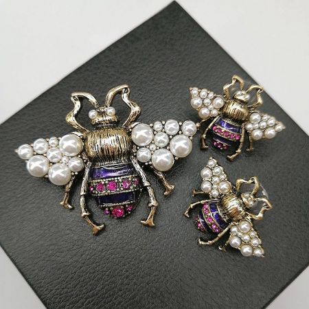 A pair of vintage bee brooches with pearl wings and purple enamel bodies, showcasing the intricate design.