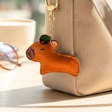 A cute handmade leather capybara keychain hanging from a beige canvas tote bag.