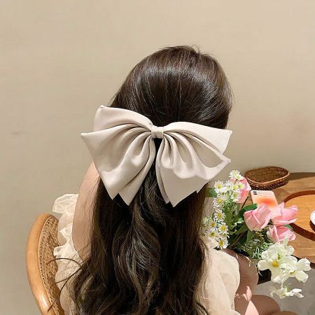 Close-up of a woman wearing a large beige ribbon bow hair clip.