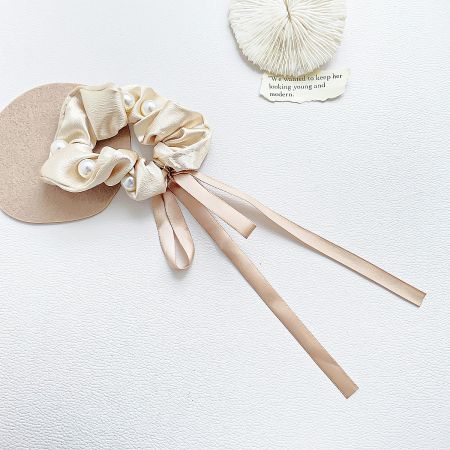 The elegant beige silk scrunchie featuring a long, flowing ribbon and delicate pearl embellishments.