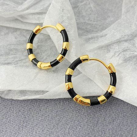 Close-up of a stylish black and gold enamel hoop earring, highlighting the sleek and modern design.