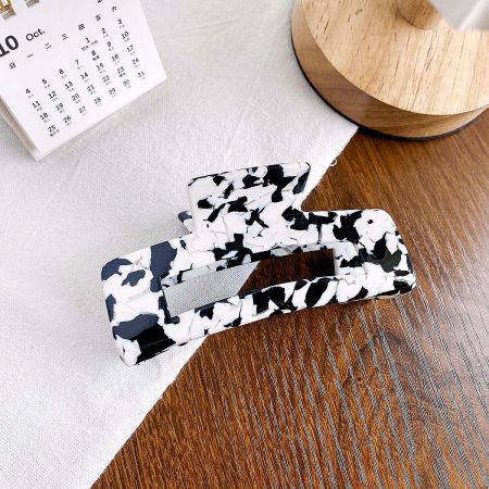 A trendy black and white cow-print square hair clip on a neutral background.