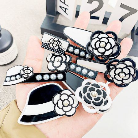 A hand holding a selection of black and white hair clips, showcasing their size and intricate pearl details.