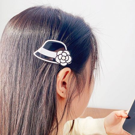 A chic black and white hat-shaped hair clip with an elegant flower accent, perfect for a sophisticated look.