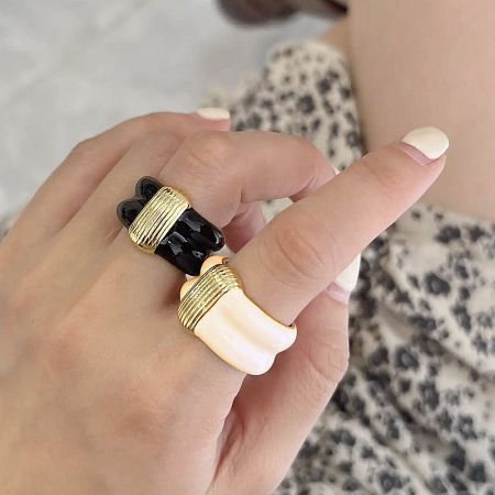 A hand model showcasing the black and white enamel rings with elegant gold accents.