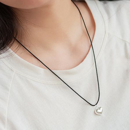 A clear shot of the silver heart pendant on the adjustable black cord.