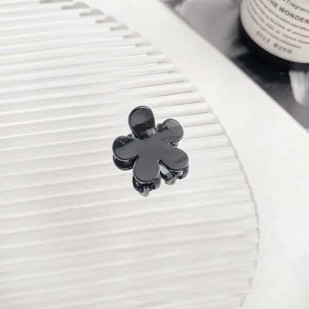 A detailed macro shot of a black four-leaf clover mini hair clip on a white surface.