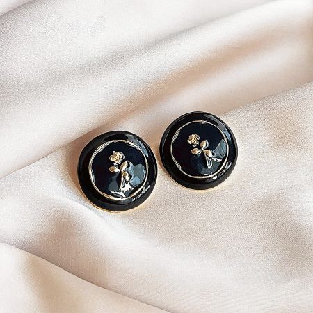 A pair of black enamel stud earrings from the set, adorned with a charming gold bow pattern.