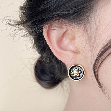 Detailed close-up of the round earring with its intricate black and gold flower design.
