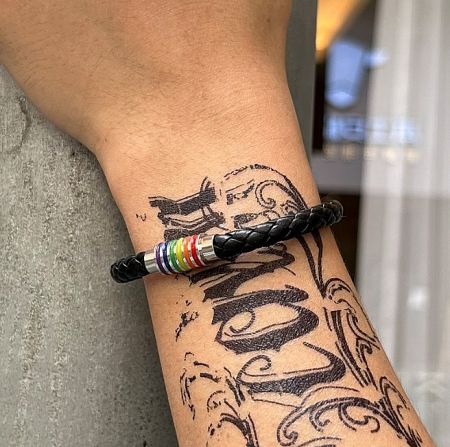 A man with a tattooed arm wearing the black PU leather bracelet with a distinctive rainbow clasp.