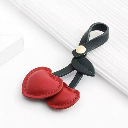 Close-up of a black leather keychain featuring a vibrant red cherry PU leather charm.
