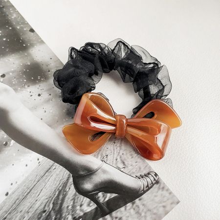 Close-up of a black scrunchie with a vibrant orange acetate bow.
