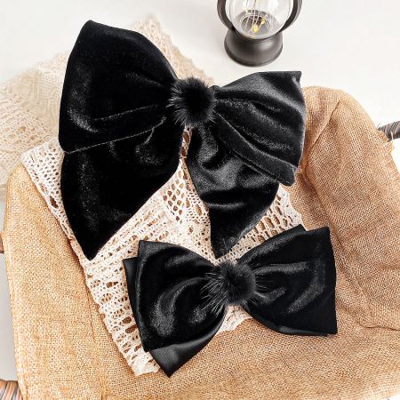 Two black velvet bow hair clips with pom-poms displayed side-by-side.