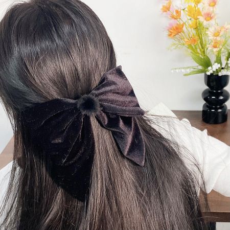 Black velvet hair bow being worn to style long dark hair.