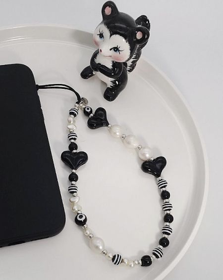 Close-up of a black and white beaded phone charm strap with a cute cat figurine, displaying the detailed craftsmanship.