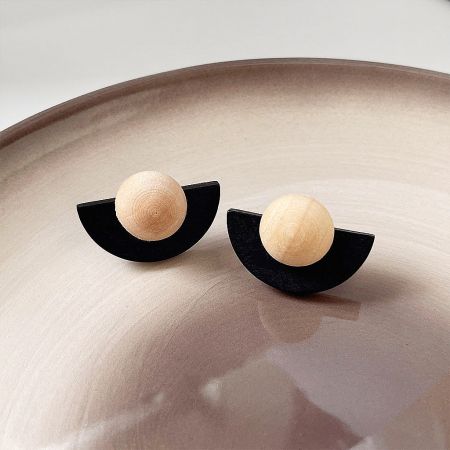 The black and wood fan-shaped earrings displayed elegantly on a textured beige ceramic plate.