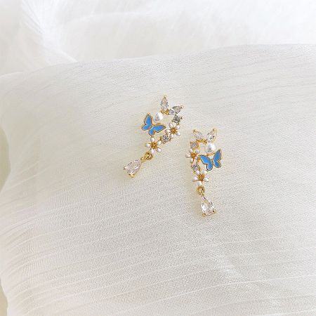 Detailed shot of the blue butterfly gold earrings, highlighting the crystal and pearl embellishments.