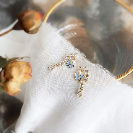 A pair of blue butterfly and pearl drop earrings displayed against a clean white background.