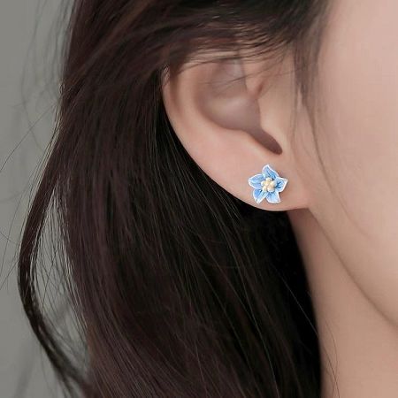 Close-up view of the dainty blue blossom earring on an ear, highlighting the delicate petal details.
