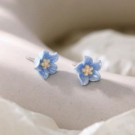 A pair of lightweight sterling silver floral earrings in pastel blue, showing the silver posts.