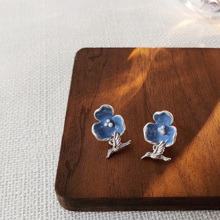 A pair of blue flower stud earrings with silver details displayed on a wooden surface.