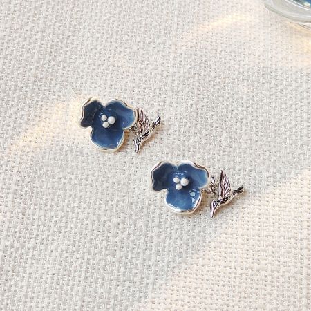 Detailed view of the blue flower and hummingbird earring design.