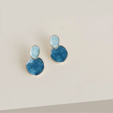 Detailed product shot of the blue and gold enamel earrings against a neutral background.