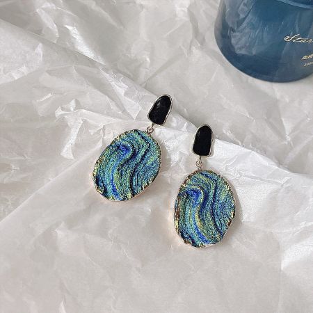 Detailed shot of a drop earring with a blue and green marbled pattern, gold border, and black accents.