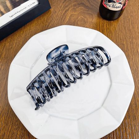 A sleek, solid black hair claw clip on a white plate.